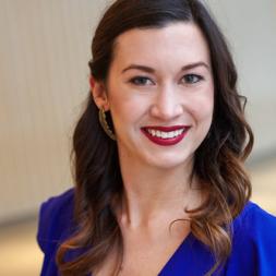 Beth Larson head shot. Woman smiling with long dark hair and wearing a blue blouse.
