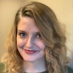 Breanne Chase headshot. Woman smiling with wavy blond hair. She is wearing a green shirt.