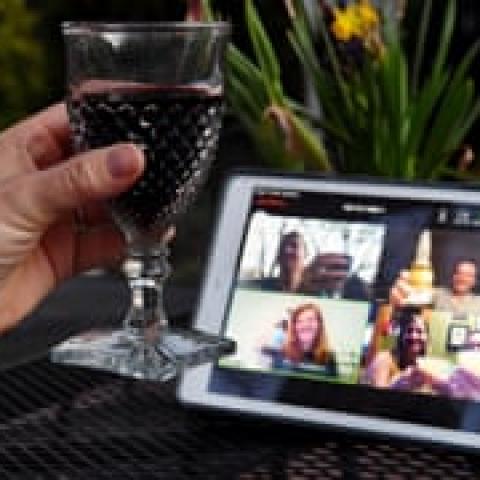 A hand holding a wine glass with a computer