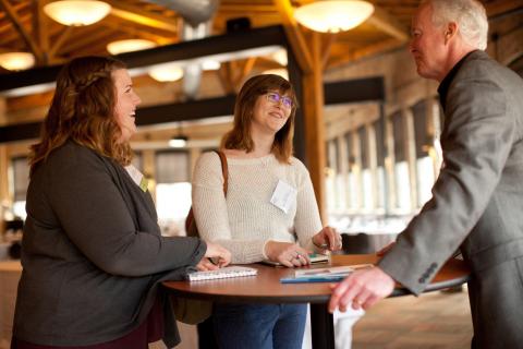 Two women speaking to a man while standing around a high top table.