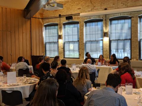 Wide room view with panelist speaking near tall windows.