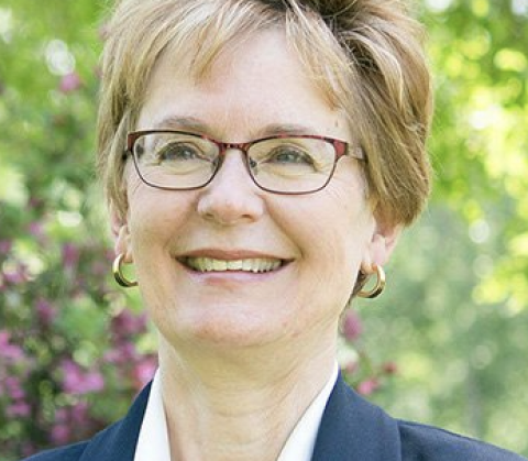 Marta Weldon. Woman smiling with short blonde hair and wearing glasses. She is wearing a blue blazer and white collar shirt.