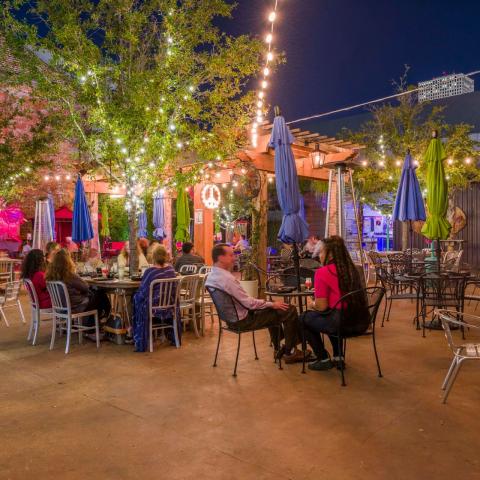 Outdoor restaurant patio with tables, trees and evening lighting.