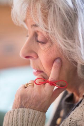 An older woman resting her head on her hand. A red ribbon is tied on her pointer finger.