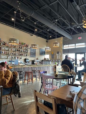 A bright room with tables with people sitting at them. Along the back wall is a full bar