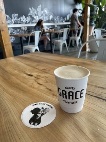 A paper coffee cup sitting next to coaster on a wood table.