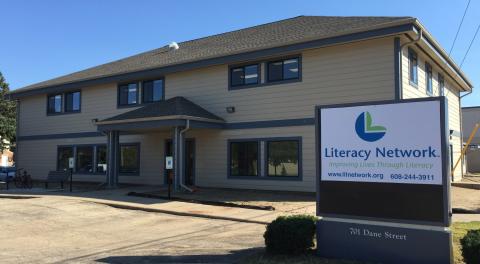 A tan building two stories tall sits in the background. A sign in front reads "Literacy Network"