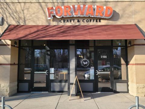 An image of a storefront with the business name written in red writing above a red awning. It says Forward Coffee.