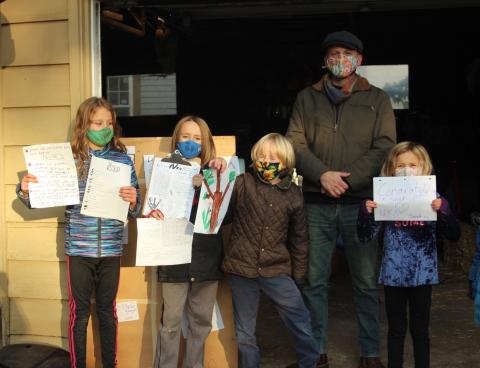 NKN group of four kids and an adult. The children are holding up signs all individuals are dressed in warm clothes and masks.