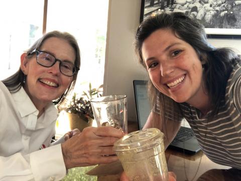 Two women smiling and giving a cheers with their beverages.