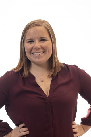 A headshot photo of a woman with short blonde hair smiling and wearing a maroon blouse.