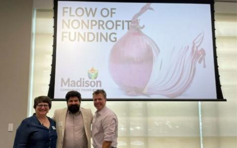 Three people, a woman on the left and two men standing in front of a screen that reads "Flow of Nonprofit Funding"