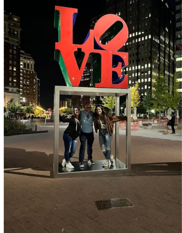 Three people standing below a large cutout sign that reads "LOVE"