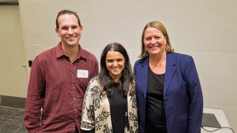 Three people posing and smiling for the camera. Far left is a man with two women standing next to him.