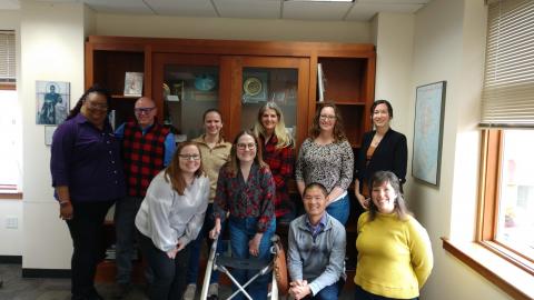 Group of people all smiling and standing in front of a book case. Four people are kneeling in the front row and six people are standing in the back row.