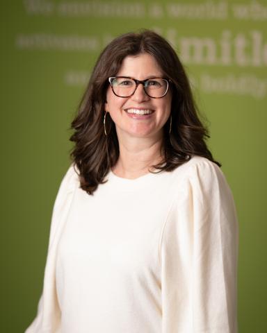 A headshot photo of a woman with shoulder length dark hair. She is wearing glasses and a white blouse.