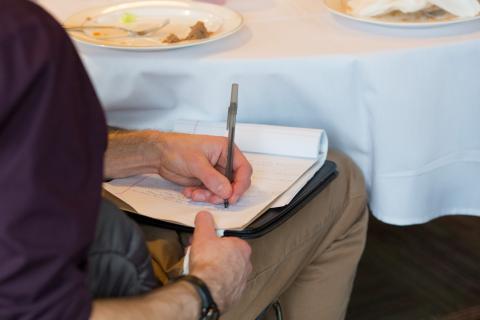 Man sitting down writing on a piece of notebook paper.