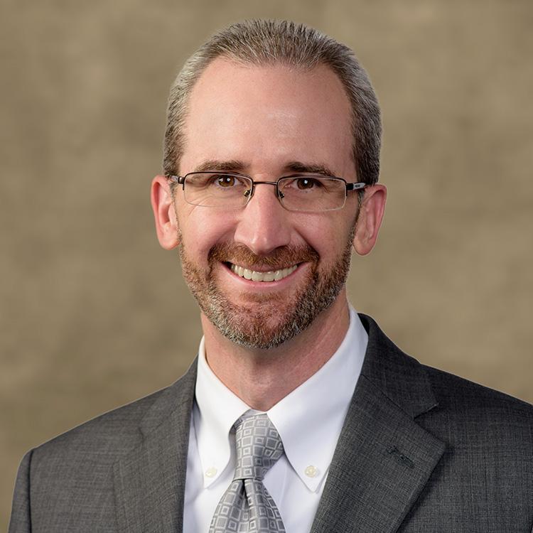 Clint Walz. Man smiling wearing glasses, a beard, and a suit and tie.